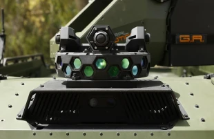 Close-up of an IAI OTHELLO-P Gunfire Detection System mounted on a military green vehicle, showcasing multiple lenses, sensors, hexagonal openings, and a central camera at the top.