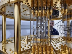 Close-up view of the intricate interior of a quantum computer, featuring gold-colored components, wires, and connectors, with a person blurred in the background.