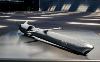 A gray, unmanned missile or drone with small wings is displayed on a flat surface inside a large, well-lit industrial space.