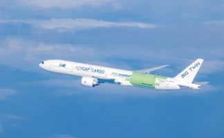 A white cargo Boeing 777-300ER with green engine covers and the words AEGCAP CARGO and BIG TWIN on the fuselage soars above, maintained by Marana Aerospace Solutions, in a blue sky with scattered clouds.