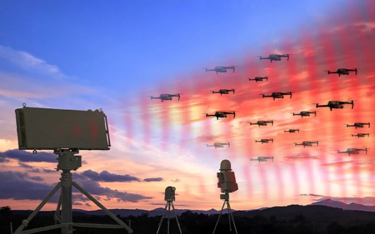 Three ground-based radar or tracking systems, possibly monitoring IAI drones, point toward a sky filled with multiple flying drones at sunset, with colorful beams indicating detection or communication. Hills and clouds are visible in the background.