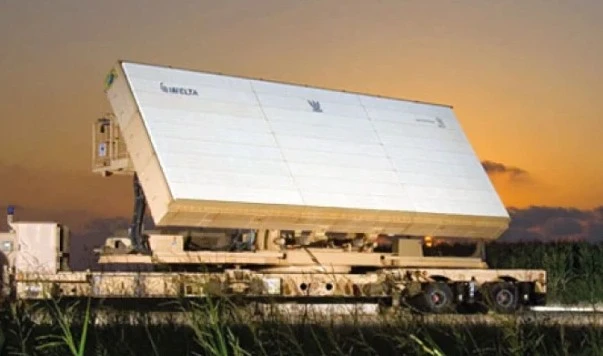 A large, rectangular IAI military radar system mounted on a trailer is seen outdoors at sunset, surrounded by grass with a clear sky in the background.