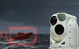 A white marine surveillance camera scans the ocean as a red digital overlay highlights a small inflatable boat with people onboard against a dark, cloudy sky.