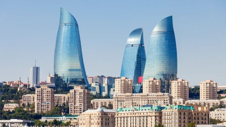 Three modern, glass skyscrapers shaped like flames rise above a cityscape of beige, historic-style buildings under a clear blue sky.