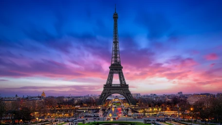 The Eiffel Tower in Paris stands tall against a vibrant sunset sky with hues of pink, purple, and blue, overlooking the city and bustling streets below.