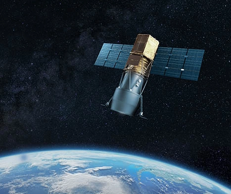 A satellite with large solar panels orbits above Earth against a backdrop of dark outer space and distant stars, with part of the planet visible below.